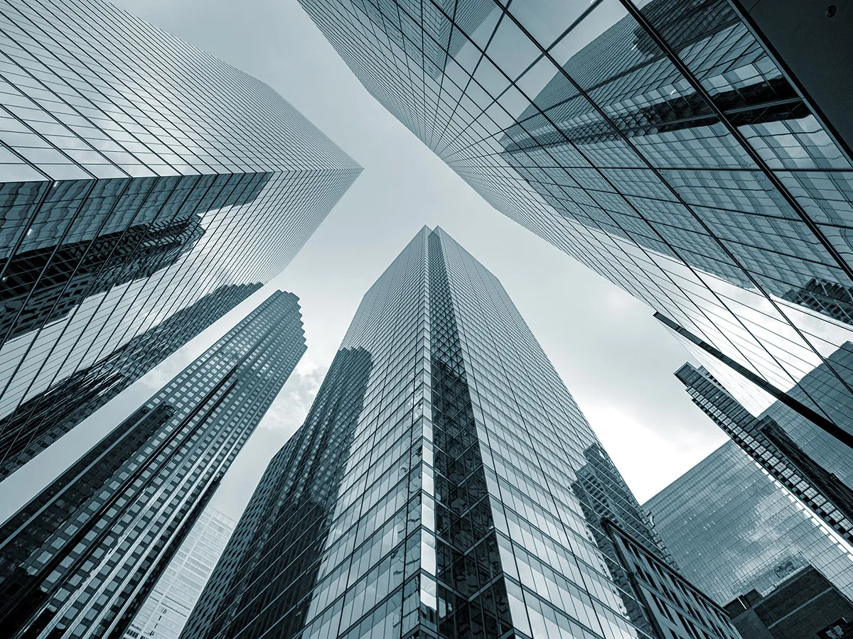 Upward view of modern skyscrapers with reflective glass facades against a cloudy sky, creating a symmetrical and geometric pattern.